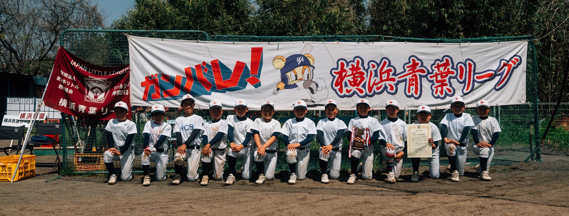 横浜青葉リーグの横断幕の前で、トロフィーと賞状を手に並ぶ選手たち